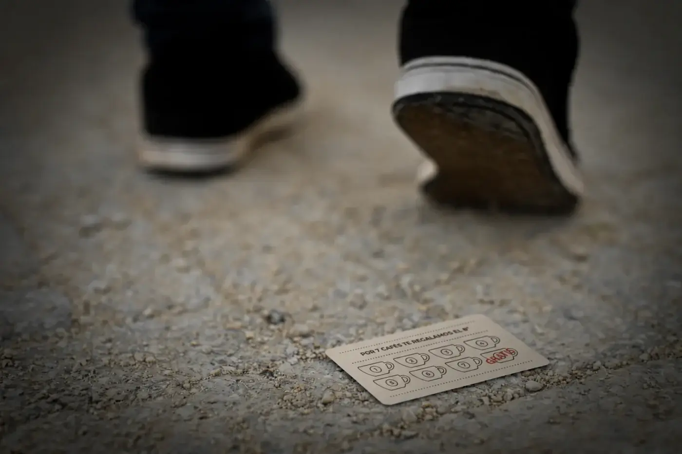 Una tarjeta de sellos de cartón tirada en el suelo de la calle, mientras los pies de una persona se alejan
